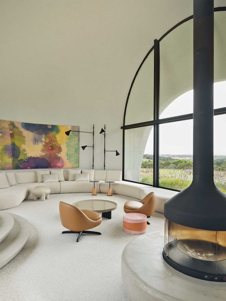 Handverputzte Wände und ein weicher Teppich aus 100 Prozent melierter neuseeländischer Wolle erden das Setting. Couchtisch und Sessel von Minotti mit einem glasierten Terrakotta-Beistelltisch von Paola Lenti markieren die Mitte des Raums. Davor spannt ein Kamin von Focus auf einer massgefertigten Betonbank die Kurve des Sofas weiter, im Hintergrund das Auftragsgemälde «Waterlyness» von Lara Merrett, flankiert von Wandleuchten von De Padova über einem Einbauschlafsofa mit Pouf von Anomaly.