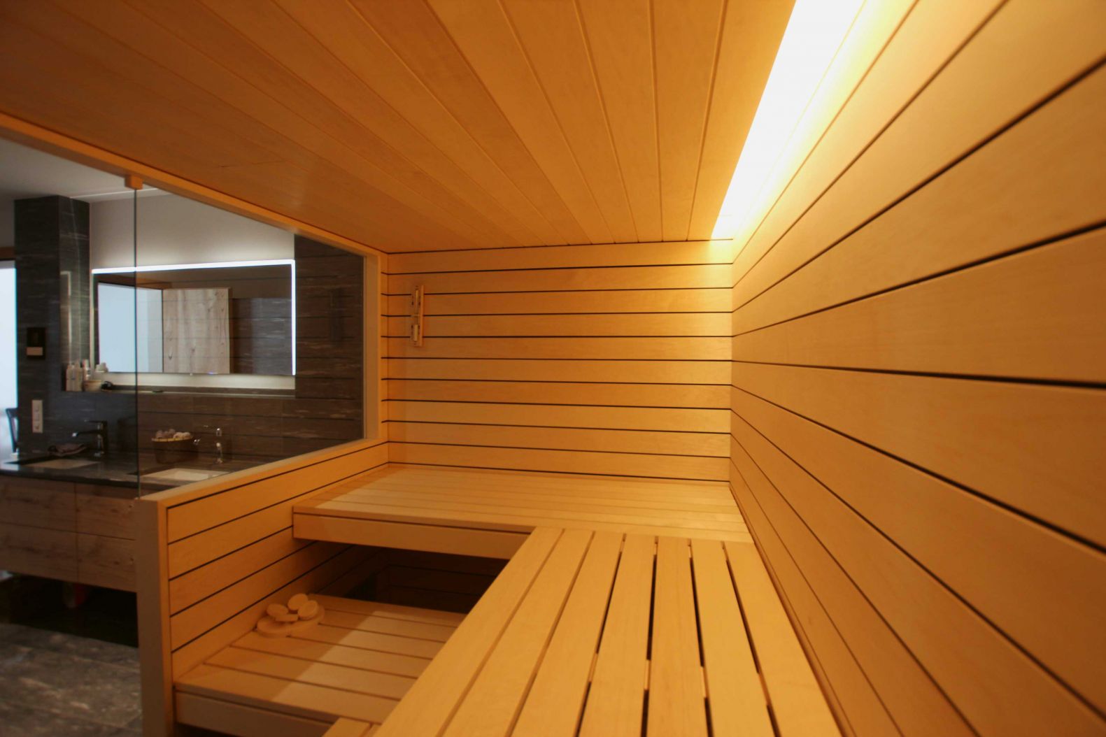 Bio-Sauna nach Mass: Offen und transparent durch Glas, stimmungsvoll durch indirekte Beleuchtung mit LED-Spots warmweiss in der Decke, Espentäfer und Bänke in heller, moderner Anmutung und ein Kombiofen für verschiedene Anwendungen: Massgeschneiderte Saunakonzepte sind die Spezialität des angesehenen Familienbetriebes. saunabau.ch