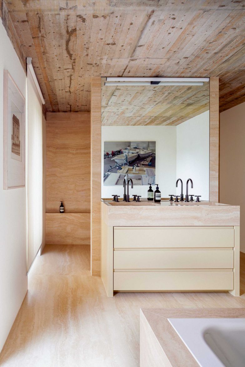 Die Dusche ist mit italienischem Travertin Romano ausgelegt, die Armaturen der Serie «Tara» in Dark Platinum gebürstet, stammen von Dornbracht. Im Badezimmer hängt das Gemälde «Boat in Workshop» (2008) von Kevin Cosgrove an der Wand. © 2022 Artists Rights Society (ARS), New York / IVARO, Dublin