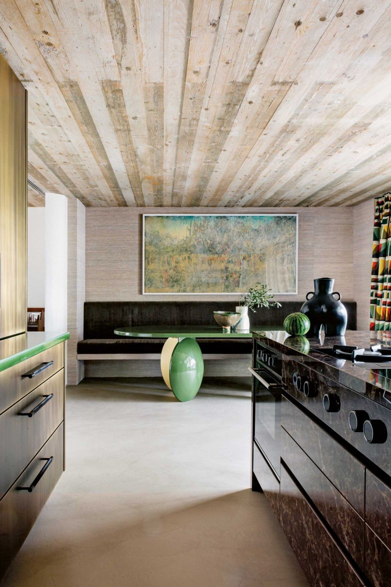 Die Küche gehört zu den Lieblingsräumen der Innenarchitektin. Die Fronten sind aus gebürstetem Messing, die Kücheninsel ist aus dunklem, spanischem Marmor. Die Holzdecke gehört zum ursprünglichen Bestand. Für den Boden kam neu der fugenlose, mineralische Spachtelbelag Texolit Rustico zum Einsatz. Der grüne Tisch, auch «Roger Table» genannt, wurde von Victoria-Maria Geyer entworfen. Das Gemälde «Creation Deterioration Conservation» (2017) ist von Pamela Rosenkranz.